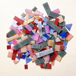 May include: A collection of assorted mosaic glass tiles in various shapes and sizes, featuring a color palette of red, pink, blue, grey, and beige. The pieces include rectangles, triangles, and irregular shards with smooth and textured surfaces.