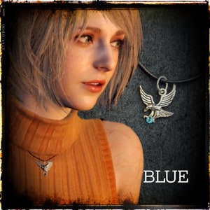 May include: A woman with short blonde hair wearing a brown sleeveless top with a silver necklace featuring a bird pendant with a blue gemstone. The word "BLUE" is written in white letters on a black background.