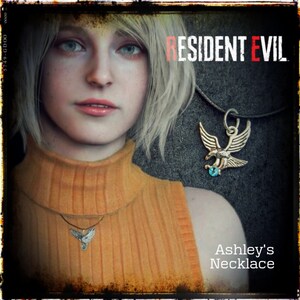 May include: A close-up of a silver eagle pendant necklace with a blue gemstone. The necklace is worn by a woman with blonde hair. The text "RESIDENT EVIL" and "Ashley's Necklace" is visible in the image.