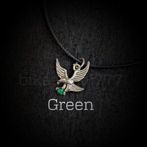 May include: A silver eagle pendant necklace with a green gemstone. The necklace is on a black cord.