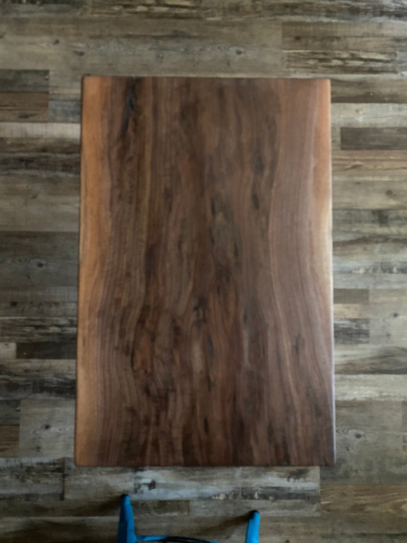 May include: A large, rectangular slab of dark brown wood with a natural wood grain pattern. The wood has a smooth, polished finish.