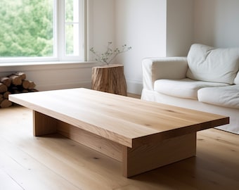 Puede incluir: Una mesa de centro de madera clara con un diseño rectangular simple. La mesa tiene una superficie ancha y plana y una sola base gruesa.