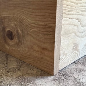 May include: Close-up of a corner of a wooden box with a knot in the wood grain. The wood is a light brown color.