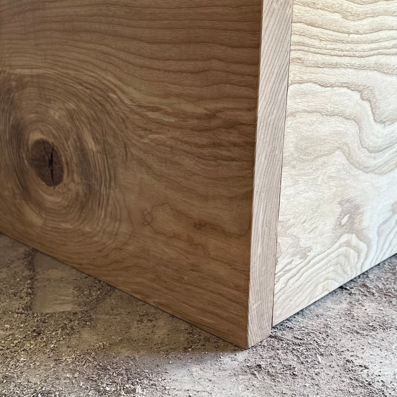 May include: Close-up of a corner of a wooden box with a knot in the wood grain. The wood is a light brown color.