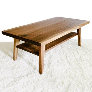 May include: A rectangular wooden coffee table with a lower shelf. The table has a natural wood finish and is supported by four legs.