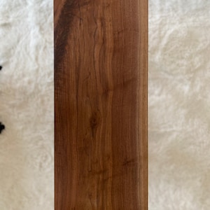 May include: A large, rectangular, wooden cutting board with a natural wood grain finish. The board has a live edge on one side and is made of walnut wood.