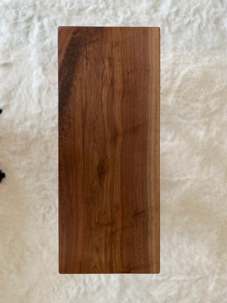 May include: A large, rectangular, wooden cutting board with a natural wood grain finish. The board has a live edge on one side and is made of walnut wood.