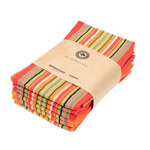 May include: A stack of kitchen towels featuring a vibrant striped pattern in orange, green, white, and blue. The towels are secured with a brown paper band labeled 100% Cotton Kitchen Towels, with a circular logo and Made in India text visible.