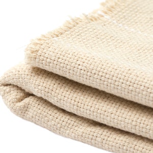 May include: A folded beige fabric with a frayed edge. The fabric has a woven texture.