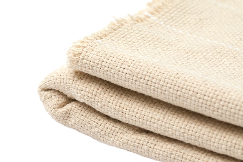 May include: A folded beige fabric with a frayed edge. The fabric has a woven texture.
