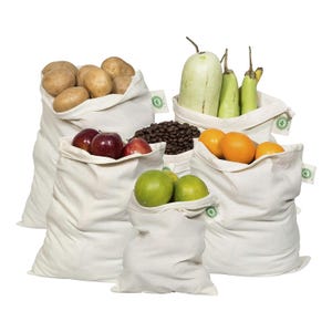 May include: A collection of five off-white cotton produce bags of varying sizes, each featuring a small green circular tag on the side. The bags are filled with assorted fresh produce including potatoes, apples, coffee beans, oranges, limes, and gourds.