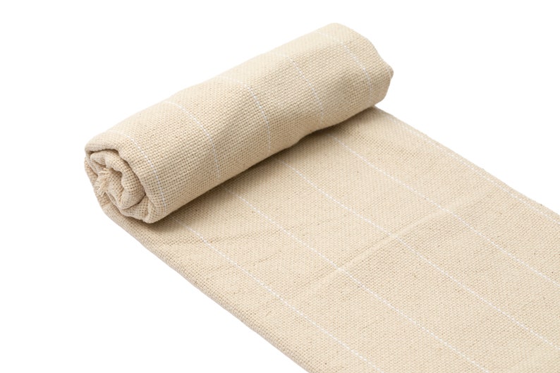 May include: A rolled up beige throw blanket with white stripes. The blanket is made of a soft, woven fabric.