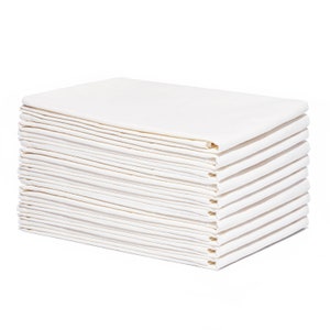 Op de afbeelding: Een stapel gevouwen, cr&egrave;mekleurige stoffen servetten. De servetten zijn netjes gerangschikt in een rechthoekige vorm, met zichtbare vouwen en randen. De stapel staat tegen een witte achtergrond, wat de schone, heldere uitstraling van de stof benadrukt.