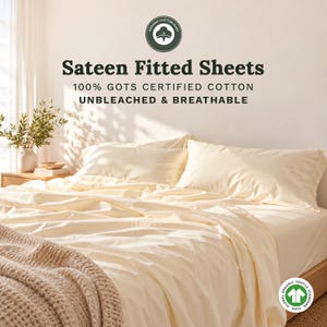 May include: Cream-colored sateen fitted sheets made of 100% GOTS certified cotton. The text reads: Organic Cotton Mart, Sateen Fitted Sheets, 100% GOTS Certified Cotton, Unbleached & Breathable. A GOTS logo is visible in the corner of the bed.
