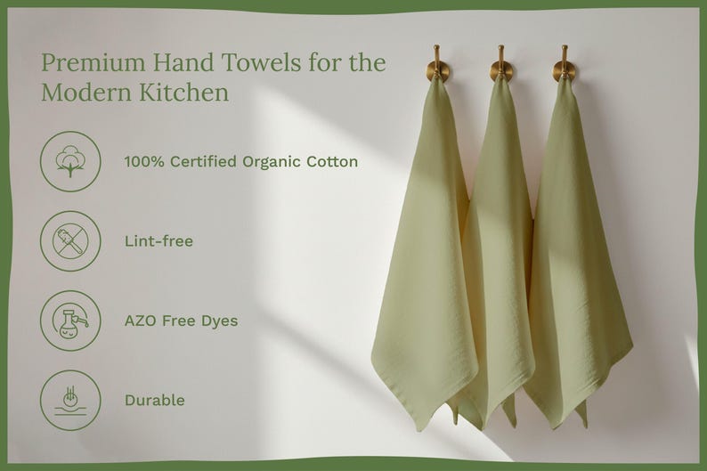 Op de afbeelding: Drie saliegroene handdoeken hangen aan gouden haken tegen een witte muur. De afbeelding bevat de tekst "Premium Hand Towels for the Modern Kitchen", "100% Certified Organic Cotton", "Lint-free", "AZO Free Dyes" en "Durable".