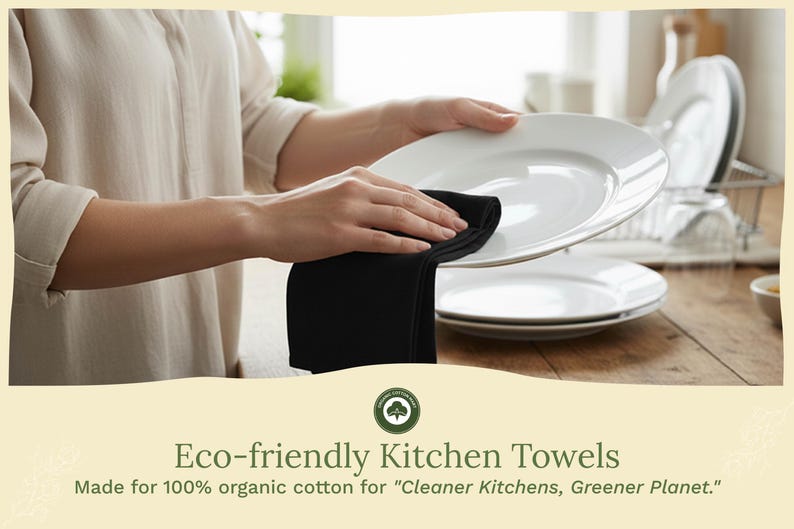 Op de afbeelding: Een zwarte keukendoek wordt gebruikt om een wit bord af te vegen. De afbeelding toont een stapel witte borden en de tekst "Eco-friendly Kitchen Towels" en "Made for 100% organic cotton for 'Cleaner Kitchens, Greener Planet.'"