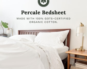 May include: A white percale bedsheet set on a dark wood bed frame. The text reads: Organic Cotton Mart, Percale Bedsheet, Made with 100% GOTS-certified organic cotton. A lamp sits on a wooden side table next to the bed with white bedding.