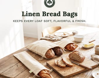 May include: Three off-white linen bread bags with drawstring closures, containing various loaves of bread. The text reads Organic Cotton Mart, Linen Bread Bags, and KEEPS EVERY LOAF SOFT, FLAVORFUL & FRESH. The bags are on a wooden table.