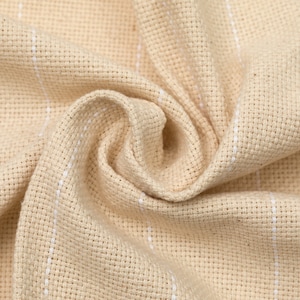 May include: Close-up of a beige fabric with white stripes. The fabric is woven and has a textured surface.