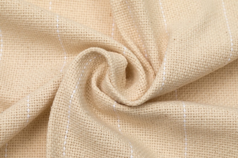 May include: Close-up of a beige fabric with white stripes. The fabric is woven and has a textured surface.