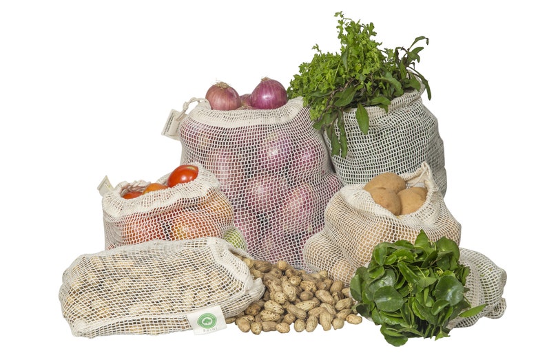 May include: A collection of off-white reusable mesh produce bags filled with various fresh items including red onions, tomatoes, potatoes, peanuts, and leafy green herbs. Each bag features a drawstring closure and a small white fabric tag.