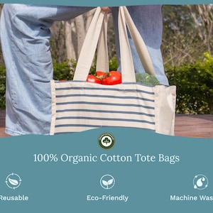 May include: A cream-colored tote bag with horizontal navy blue stripes, featuring two sturdy handles and filled with fresh red tomatoes and broccoli. The text 100% Organic Cotton Tote Bags is displayed below, along with icons for reusable, eco-friendly, and machine washable features.