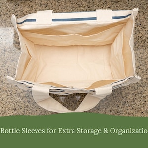 May include: An open rectangular canvas tote bag with cream-colored fabric and navy blue horizontal stripes. The interior features six internal bottle sleeves for organization. The text 6 Bottle Sleeves for Extra Storage & Organization is visible.