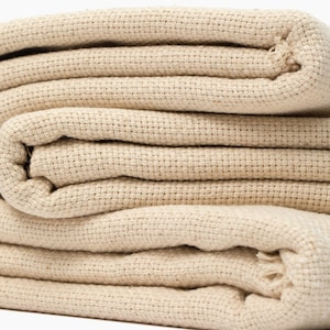 May include: A stack of folded beige canvas fabric. The fabric is woven with a tight, even weave.