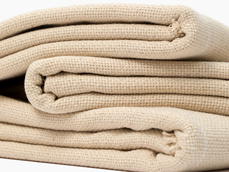 May include: A stack of folded beige canvas fabric. The fabric is woven with a tight, even weave.