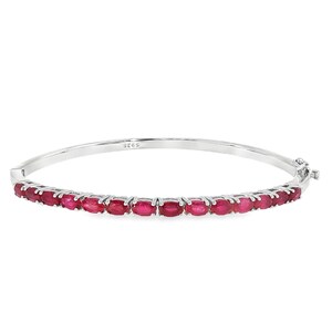 Puede incluir: Una pulsera rígida articulada de tono plateado con una hilera de piedras preciosas de color rojo intenso y corte ovalado en la mitad frontal. La banda metálica está pulida e incluye un pequeño cierre lateral, con el sello 925 en el interior.