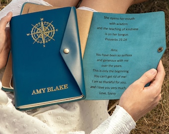 May include: A deep sea blue leather journal with a gold compass emblem and the name AMY BLAKE embossed on the front cover. The interior flap features an engraved message: She opens her mouth with wisdom and the teaching of kindness is on her tongue.
