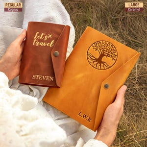 May include: Two leather travel journals, one cognac and one caramel. The cognac journal has the text "Let's travel" and the name "STEVEN". The caramel journal features a tree design and the initials "L.W.R". Both journals have a snap closure.