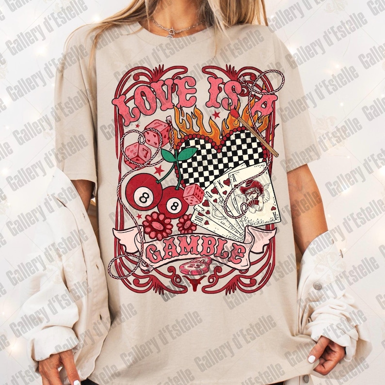 May include: Beige t-shirt with a retro graphic design. The design features the words "LOVE IS A GAMBLE" in pink, along with dice, playing cards, cherries, and a checkered heart. The shirt has short sleeves.