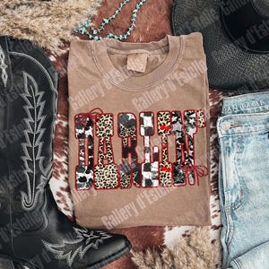 May include: A tan t-shirt with the word "DARLIN" in a decorative font with animal print and star accents. The shirt is surrounded by a black cowboy boot, a black hat, and blue jeans.
