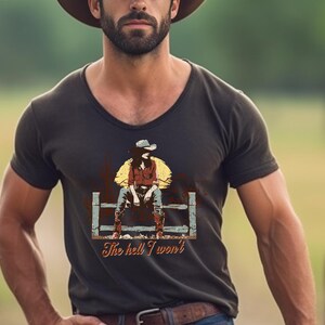 Op de afbeelding: Een donkerbruin V-hals T-shirt met een vintage afbeelding van een vrouw die een cowboyhoed draagt en op een hek zit. De tekst "The hell I won't" is onder de afbeelding gedrukt.