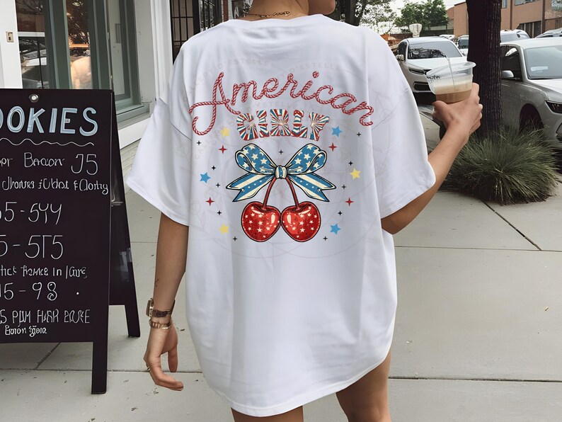 May include: White t-shirt with a red, white and blue cherry graphic and the text "American Girl" in a rope-like font.
