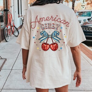 May include: A white t-shirt with a red, white and blue cherry design and the text "American Cherry" on the back.
