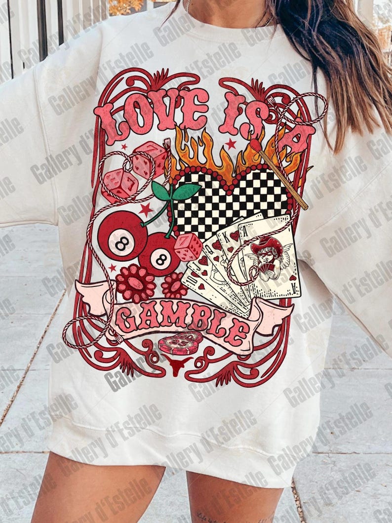 May include: White sweatshirt with a graphic design featuring the words "LOVE IS A GAMBLE" in pink, along with dice, playing cards, cherries, and an eight ball. The design has a vintage, retro aesthetic.