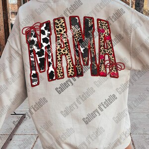 May include: Cream-colored sweatshirt with the word "MAMA" in a bold, decorative design. The letters feature various patterns, including cow print, leopard print, and star patterns, outlined in red.