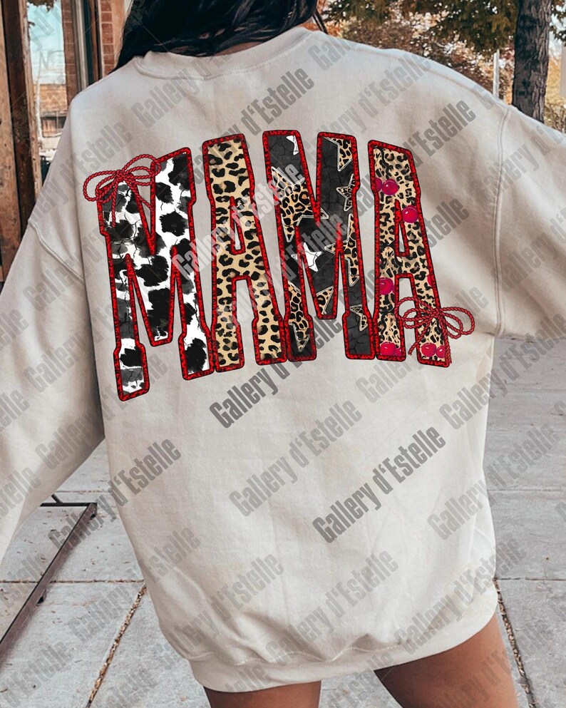 May include: Cream-colored sweatshirt with the word "MAMA" in a bold, decorative design. The letters feature various patterns, including cow print, leopard print, and star patterns, outlined in red.