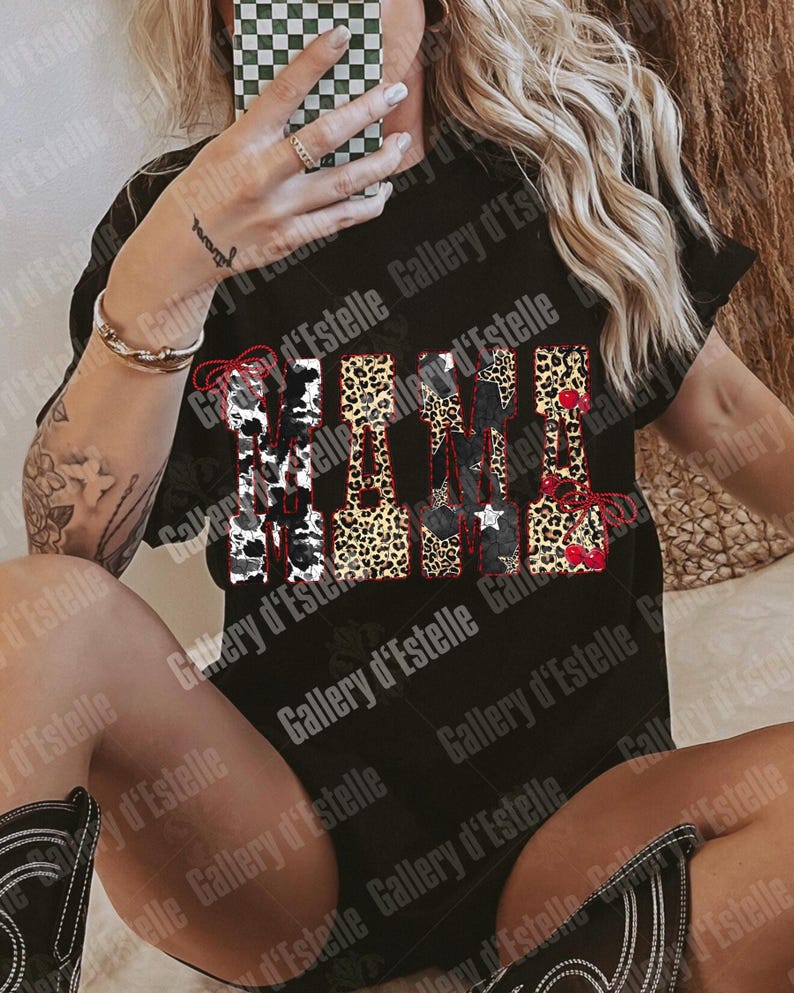 May include: Black t-shirt with the word "MAMA" in a mix of patterns: cow print, leopard print, and stars. The word is outlined in red. The shirt is a casual style.
