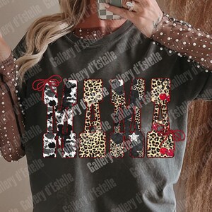 May include: Dark gray t-shirt with the word "MAMA" in a decorative font. The letters feature cow print, leopard print, stars, and cherries. The sleeves are sheer with pearl accents.
