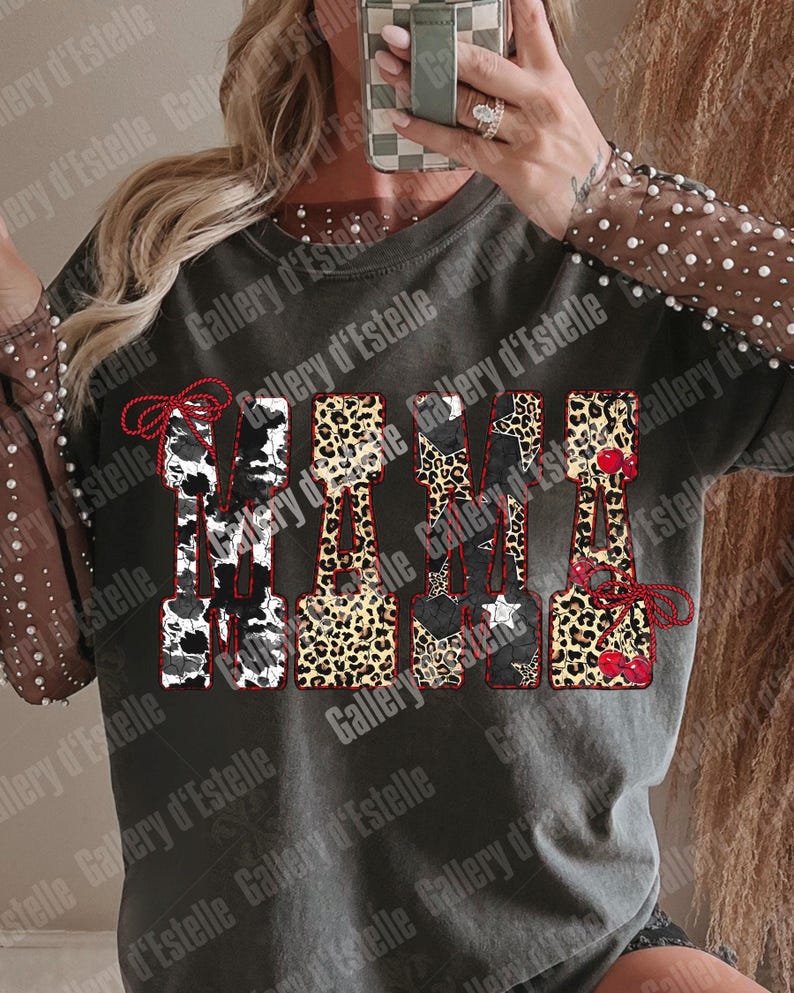 May include: Dark gray t-shirt with the word "MAMA" in a decorative font. The letters feature cow print, leopard print, stars, and cherries. The sleeves are sheer with pearl accents.