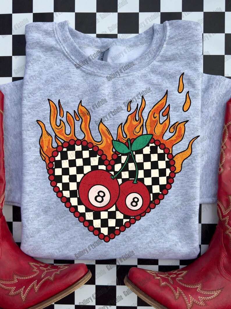 May include: A light gray sweatshirt featuring a heart-shaped design with a checkered pattern and two red 8-ball cherries. The heart is surrounded by orange flames and red beads. Red cowboy boots are on either side of the sweatshirt.