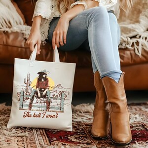 Op de afbeelding: Witte tote bag met een afbeelding van een vrouw met een cowboyhoed en de tekst "The hell I won't".