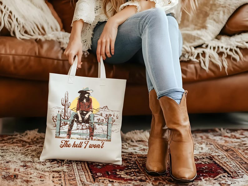 Op de afbeelding: Witte tote bag met een afbeelding van een vrouw met een cowboyhoed en de tekst "The hell I won't".