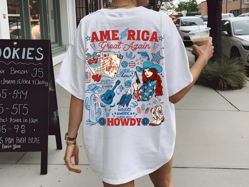 以下が含まれることがあります： アメリカ国旗をモチーフにしたグラフィックプリントが施された白いTシャツ。カウボーイハット、星、花火、そして「AMERICA Great Again... HOWDY」の文字がデザインされています。