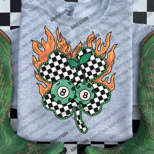 May include: A light gray sweatshirt featuring a four-leaf clover design with a checkered pattern, two eight-ball cherries, and flames. The sweatshirt is paired with green cowboy boots. The design is a St. Patrick's Day theme.