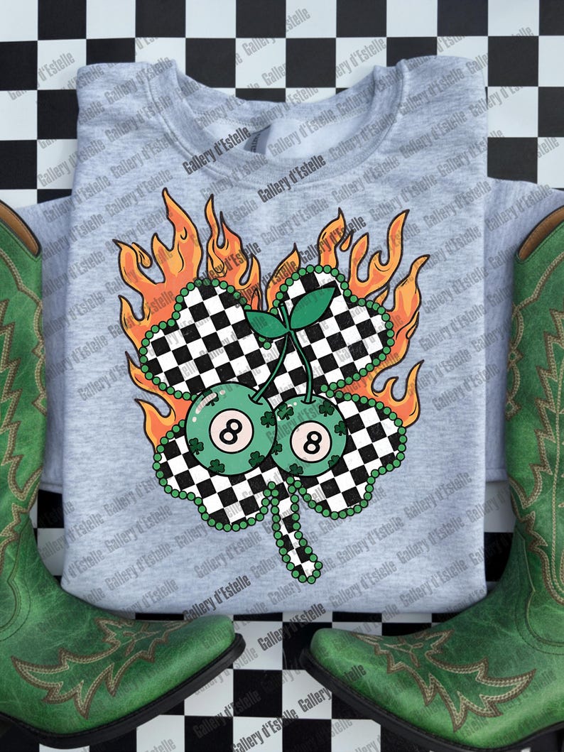 May include: A light gray sweatshirt featuring a four-leaf clover design with a checkered pattern, two eight-ball cherries, and flames. The sweatshirt is paired with green cowboy boots. The design is a St. Patrick's Day theme.