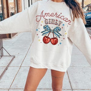May include: White sweatshirt with a red, white and blue graphic design that says "American Girl" with a cherry and bow design.